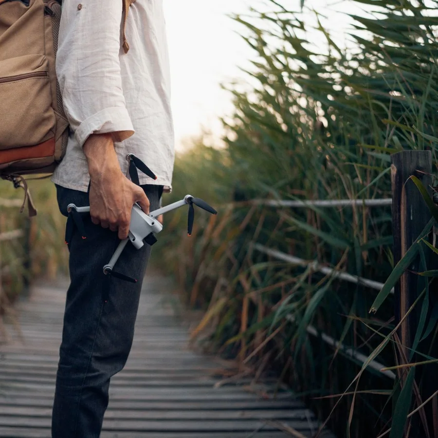 Traveller carrying a folded DJI Mini drone on a boardwalk